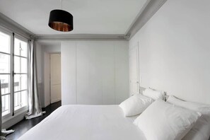 Une chambre à coucher au style minimaliste, avec un grand lit, des murs blancs et une suspension noire.