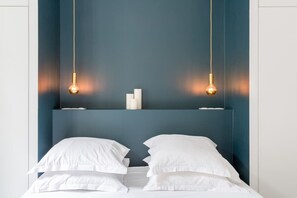 Uma cama com lençóis brancos e duas luminárias penduradas.