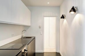 Cozinha moderna com armários brancos, bancada de aço inoxidável e torneira preta. Duas luminárias fixadas na parede à direita.