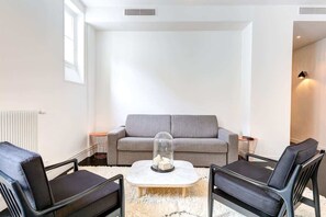 A modern living room with a grey sofa, two black armchairs, a white coffee table, and a glass dome over a decorative item.