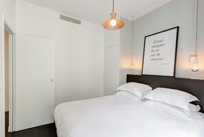 Un dormitorio con cama, una cita enmarcada en la pared, una lámpara colgante y una puerta.