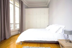 A bedroom with a bed, a nightstand, a lamp, a wardrobe, and a window with curtains.