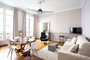 A modern living room with a dining area, a black leather chair, a white sofa, and a large mirror.