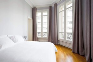 Quarto com uma cama grande, uma mesa de cabeceira e uma janela com cortinas.