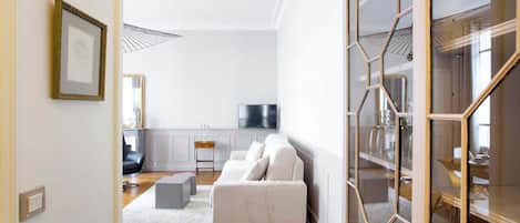 A modern living room with a white sofa, a small side table, and a flat-screen TV on a white wall.