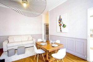 Uma sala de jantar com uma mesa de madeira posta para quatro pessoas, um sofá branco e uma luminária pendente moderna.