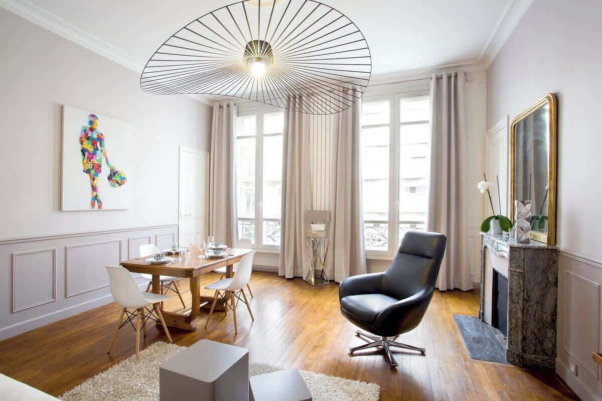 A modern living room with a dining area, a fireplace, and a large window with curtains.