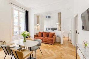 A modern living room with a sofa, a dining table with chairs, and a TV mounted on the wall.