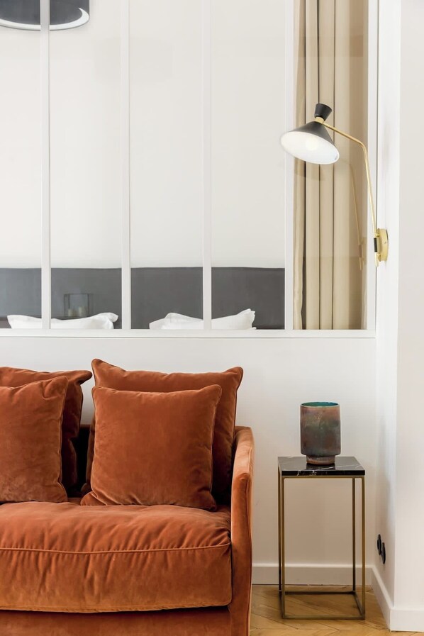 A room with a brown sofa, a small side table with a lamp, and a window with curtains.