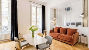 Una sala de estar moderna con un sofá blanco, una mesa de comedor con sillas y un ventanal con cortinas negras.