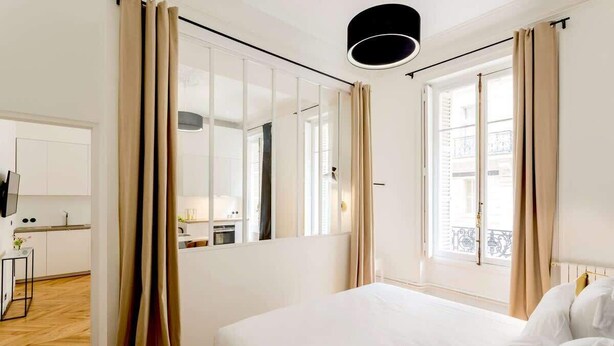 Habitación de hotel con cama, ventana con cortinas, espejo y vista al balcón exterior.