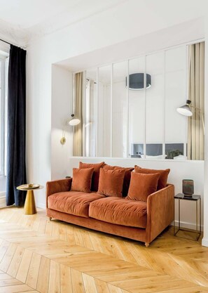 Een moderne woonkamer met een bruine bank, een klein rond tafeltje en een hoge vloerlamp.