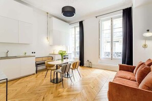 A modern kitchen with white cabinets, a dining table with chairs, and a large window with curtains.