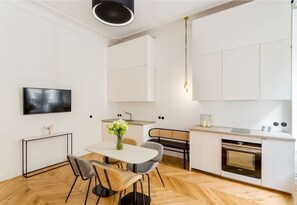 A modern kitchen with white cabinetry, a dining area with a white table and chairs, and a large window.