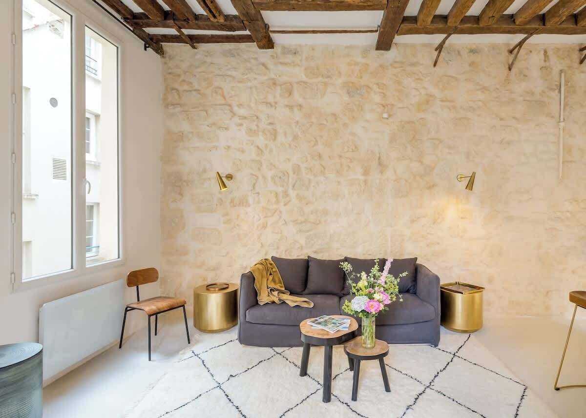 Ein gemütliches Wohnzimmer mit Steinwand, einem dunklen Sofa, einem Couchtisch und einem Blumenstrauß.