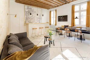 Una sala de estar moderna con sofá, comedor y ventanas amplias.