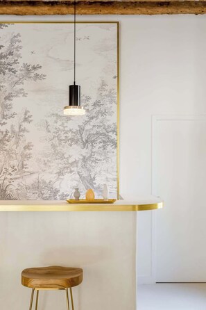 A modern kitchen with a minimalist design, featuring a large window with a nature-inspired mural, a pendant light, and a bar area with stools.