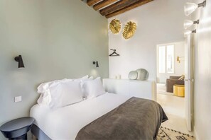 A bedroom with a bed, bedside tables, a hanging light fixture, and a door leading to another room.