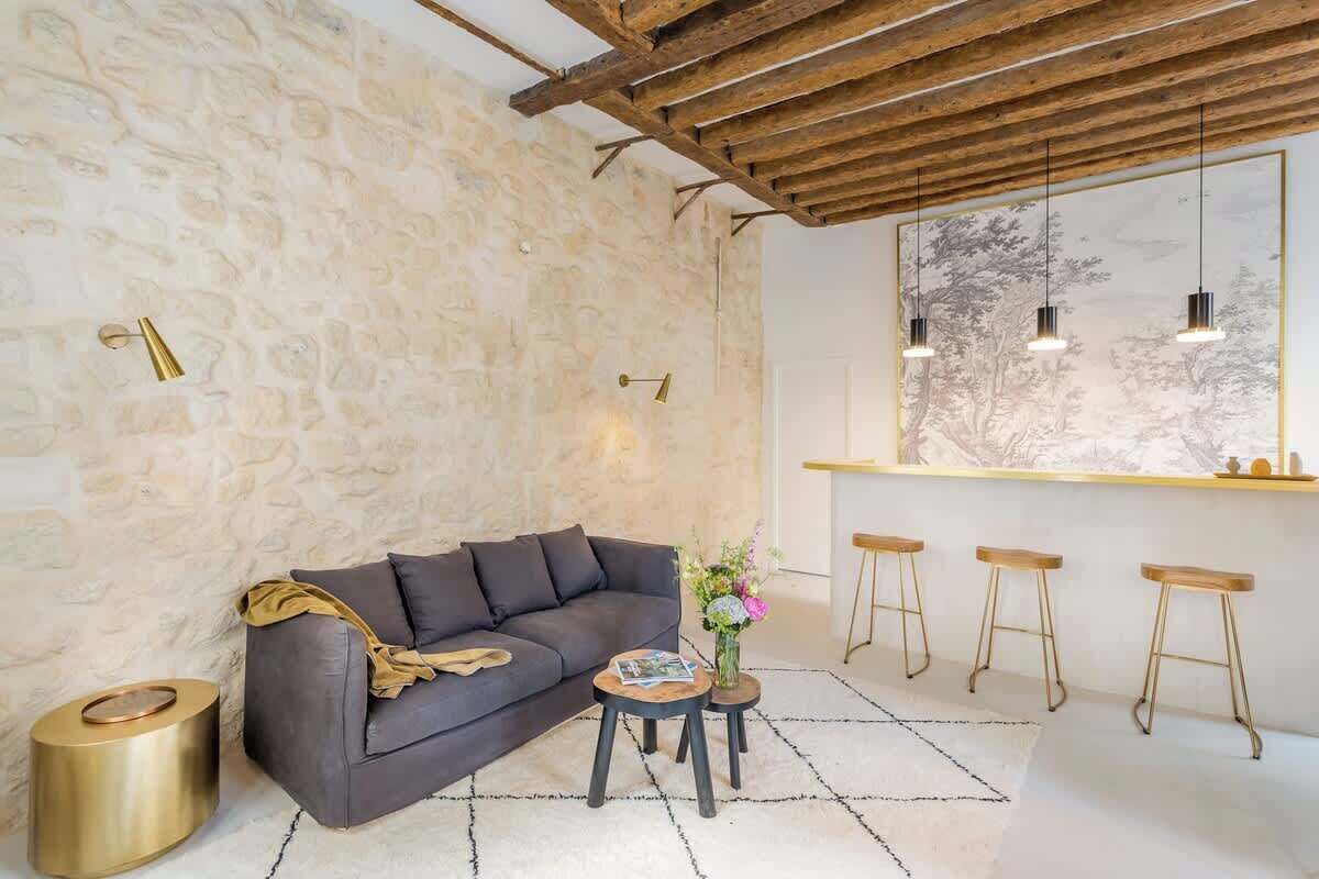 Una sala de estar moderna con una pared de piedra, un sofá gris oscuro, una mesa de centro de madera y una zona de bar con taburetes.
