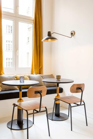 Un comedor con mesa y sillas, una ventana con cortinas amarillas y una lámpara fijada a la pared.
