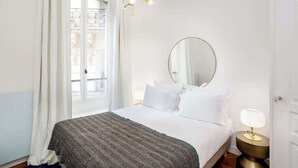A hotel room with a bed, a round mirror, a bedside lamp, and a window with curtains.