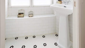 Un bagno con lavandino bianco, uno specchio e una finestra con tende bianche.