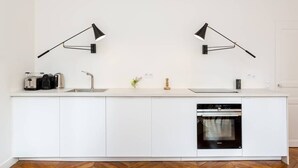 A modern kitchen with white cabinetry, a built-in oven, and two wall-mounted black lamps.