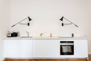 Une cuisine moderne avec des meubles blancs, un four encastré et deux lampes noires fixées au mur.