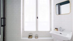 A bathroom with white brick walls, a window with a black handle, a white sink with a gold faucet, and a mirror with a gold frame.