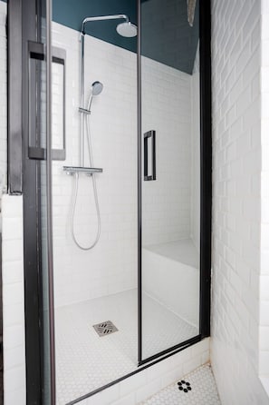 A glass-enclosed shower with a handheld showerhead and a wall-mounted faucet.