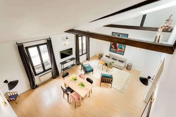 A spacious living area with a dining table, sofas, and a high ceiling with exposed beams.