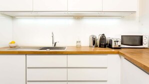 A modern kitchen with white cabinets, a wooden countertop, a sink, a kettle, a toaster, and a microwave.