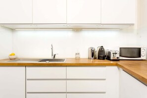 Uma cozinha moderna com armários brancos, bancada de madeira, pia, chaleira, torradeira e micro-ondas.