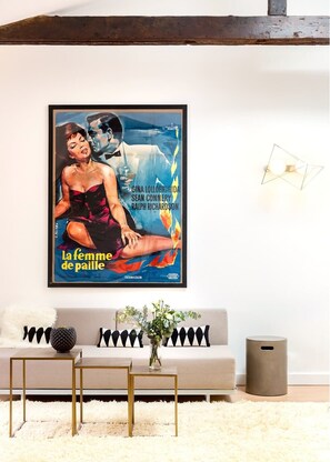 Uma sala de estar com um sofá, uma mesa de centro e um cartaz de filme emoldurado na parede.