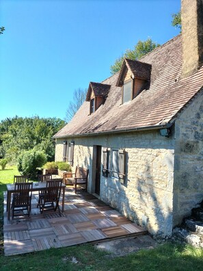 A stone building with a tiled roof, a wooden deck with chairs, and a small garden area. - Traditional Lot Cottage (ISSENDOLUS)