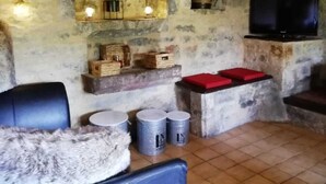 Un interior rústico con paredes de piedra, techo de madera, televisor y una zona de estar con una manta de piel.