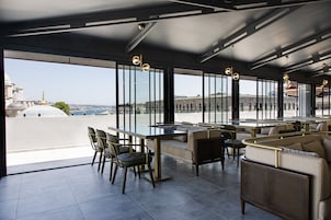 A rooftop bar with a glass table, chairs, and sofas, offering a view of the cityscape.