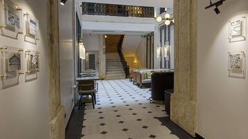 A hallway with a checkered floor, framed artwork on the walls, a staircase, and seating areas.