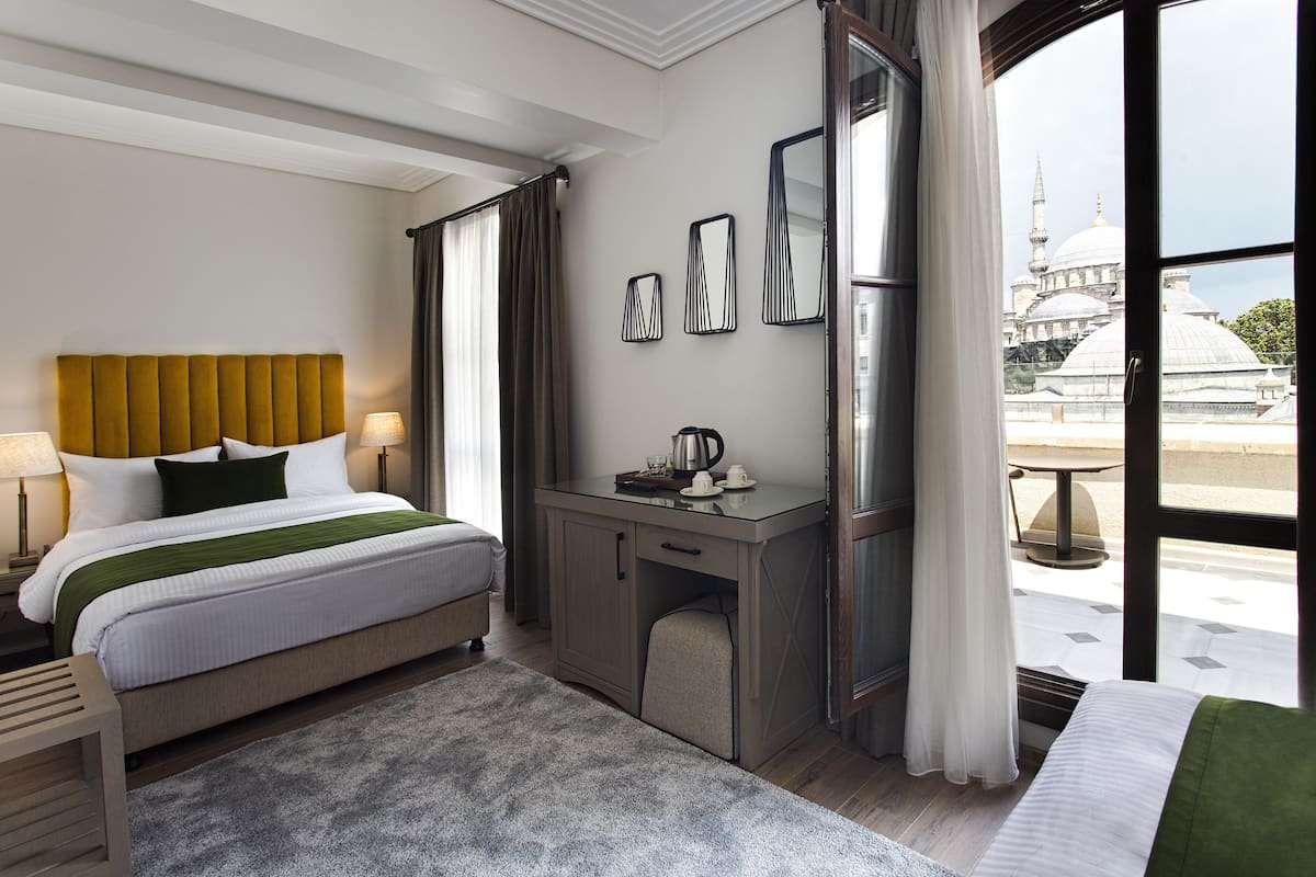Ein Hotelzimmer mit Bett, Schreibtisch und Blick auf eine Moschee durch das Fenster.