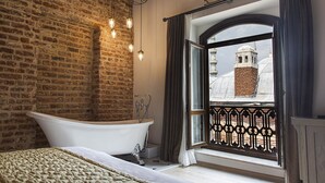 A bathroom with a freestanding bathtub, a brick wall, and a window with a view of a building. - Mest Hotel Istanbul Sirkeci (Istanbul)