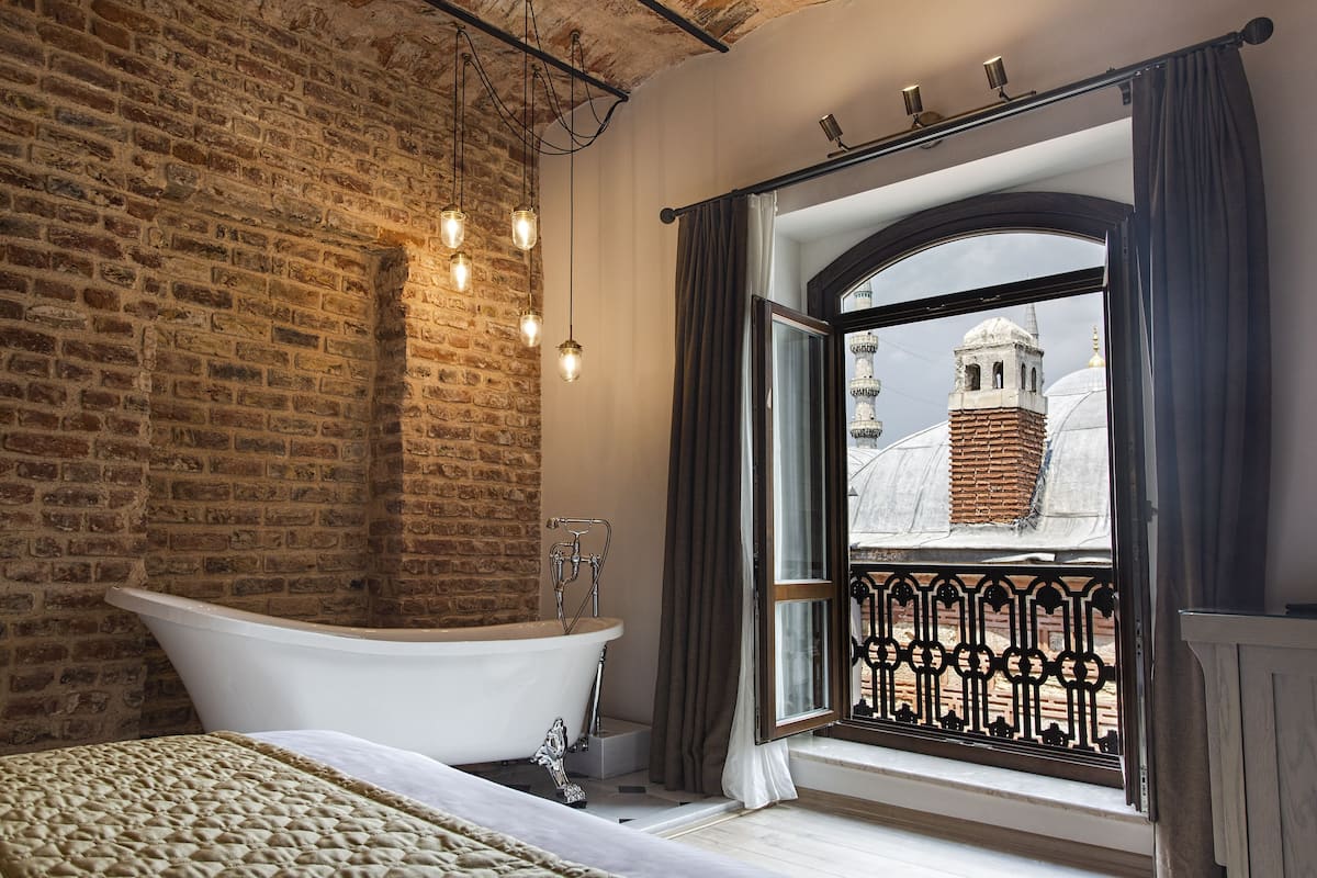 Ein Badezimmer mit einer freistehenden Badewanne, einer Ziegelwand und einem Fenster mit Blick auf ein Gebäude.