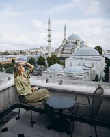 Eine Person sitzt an einem Tisch mit Blick auf eine Moschee mit zwei Minaretten und einer Kuppel im Hintergrund.