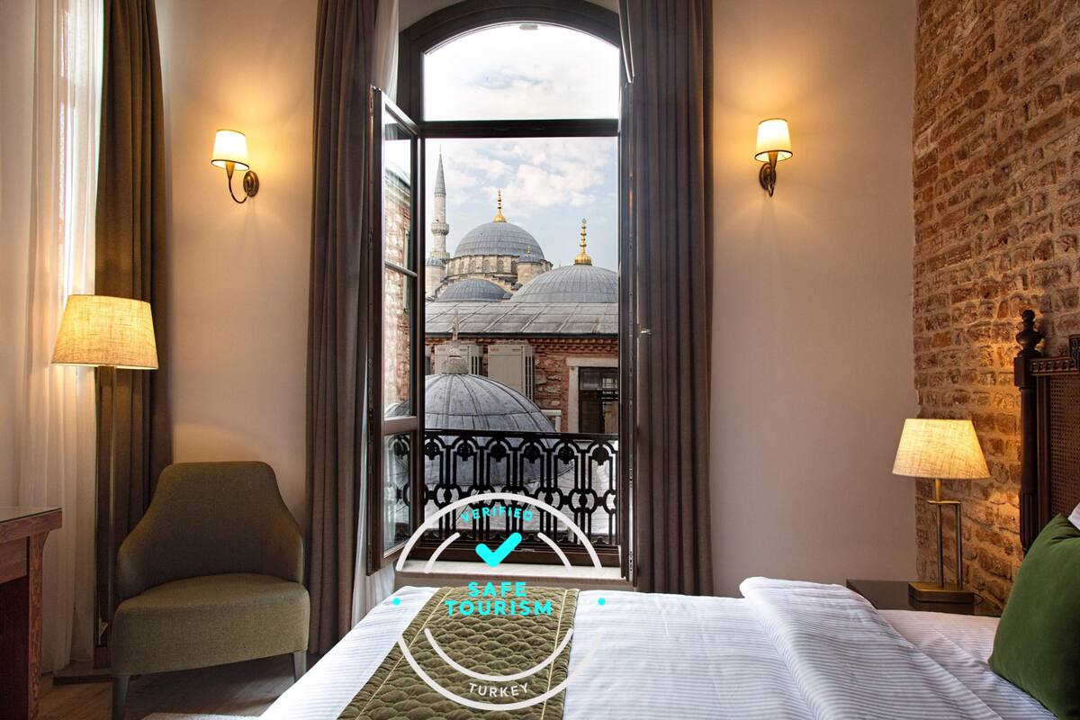 Ein Hotelzimmer mit einem Bett, zwei Lampen, einem Sessel und Blick auf eine Moschee mit Kuppeln.
