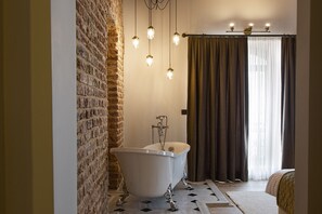 A bathroom with a freestanding bathtub, a brick wall, and a large window with curtains.