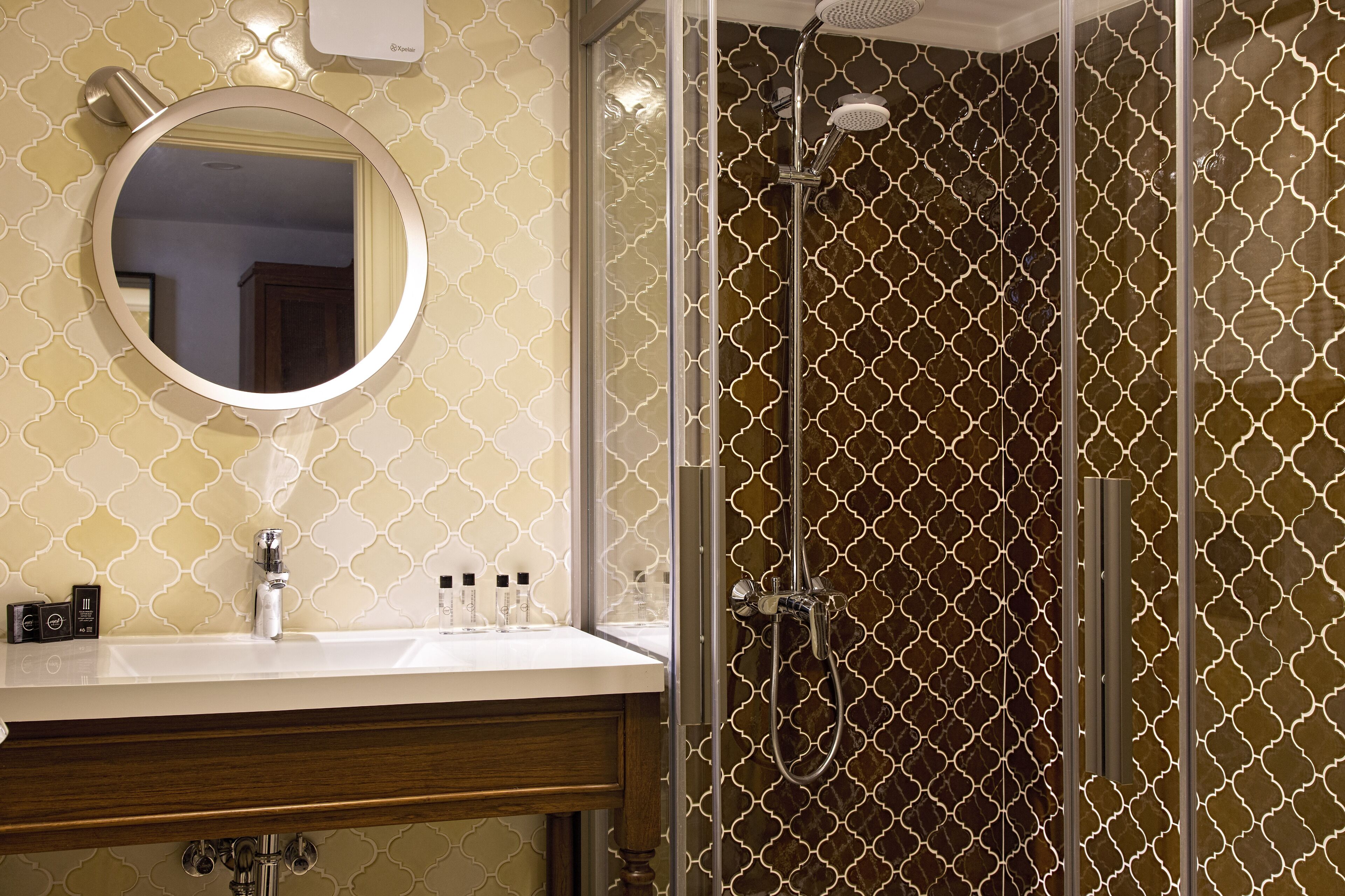 Une salle de bain avec un miroir rond, un lavabo avec des articles de toilette et une douche à parois de verre.