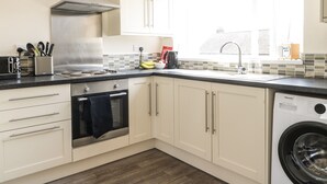 Une cuisine moderne avec des armoires blanches, une hotte de cuisinière en acier inoxydable, un four encastré, un lave-vaisselle et une fenêtre qui laisse entrer la lumière naturelle.