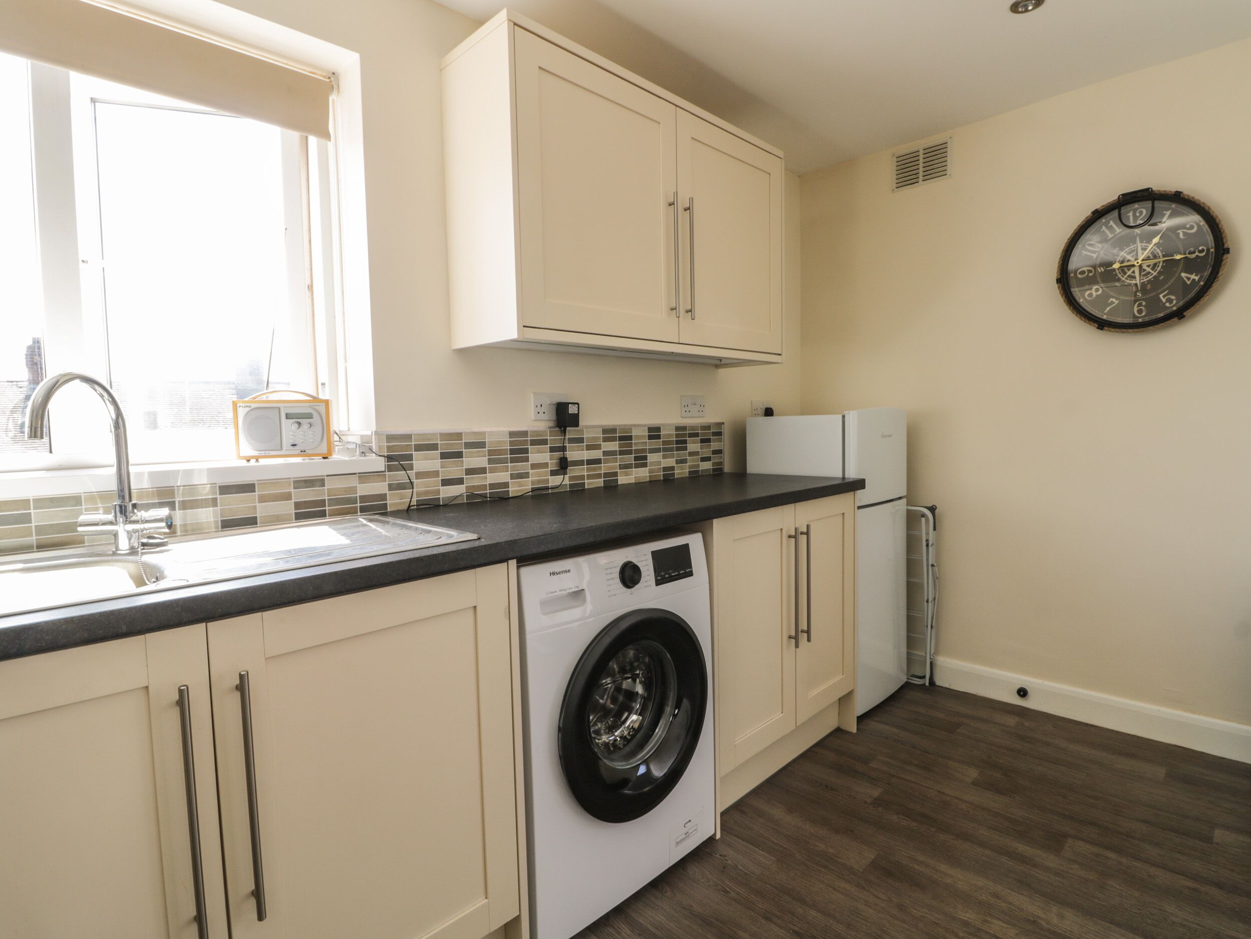 A compact kitchen with a washing machine, a refrigerator, and a clock on the wall.