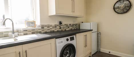 A compact kitchen with a washing machine, a refrigerator, and a clock on the wall.