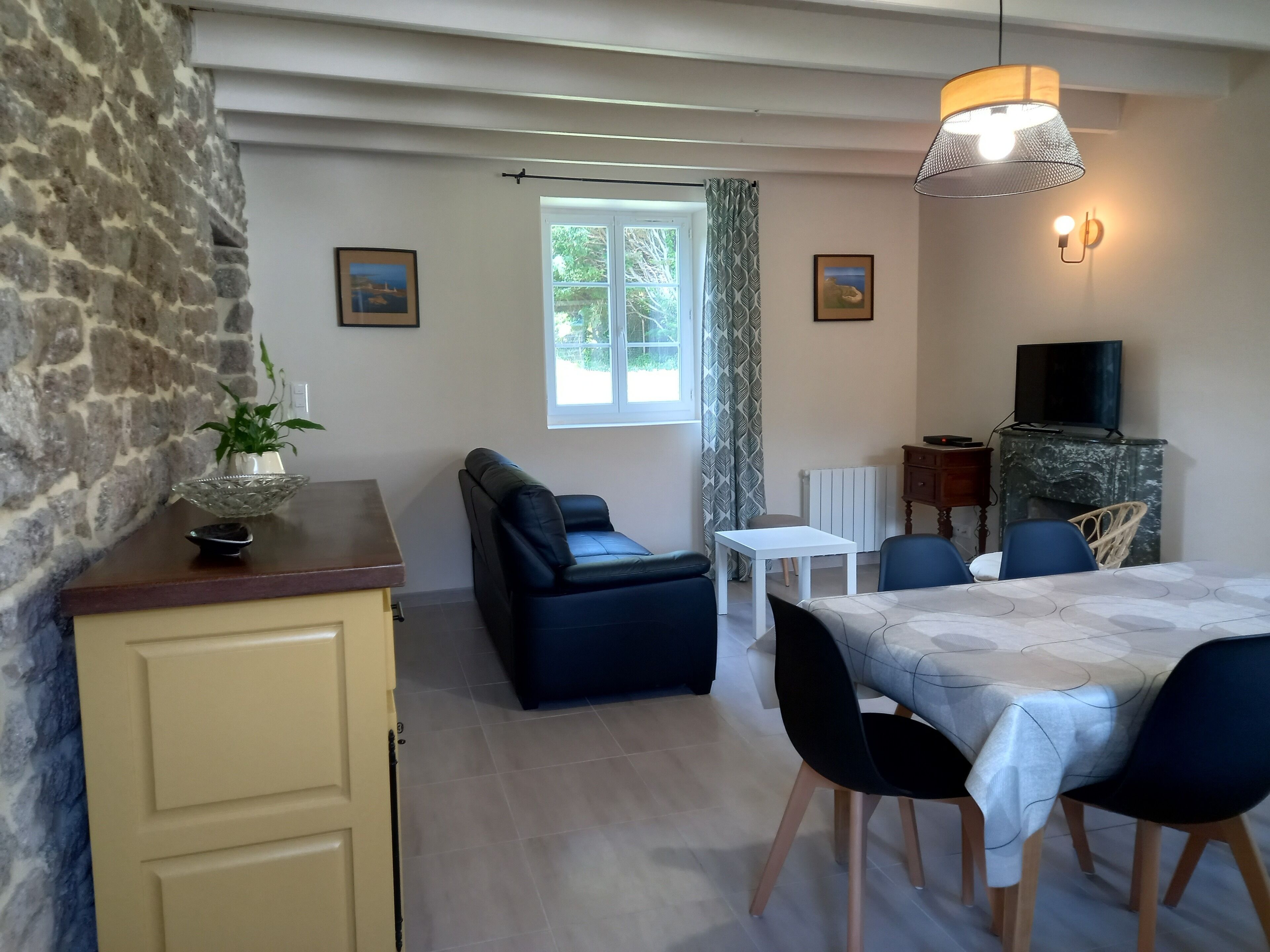 Ein gemütliches Zimmer mit Steinwand, einer Couch, einem Esstisch mit Stühlen, einem Fernseher und einem Kamin.