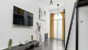 Una sala moderna con un televisor de pantalla plana, un banco con adornos decorativos, una escultura y un ventanal con cortinas.
